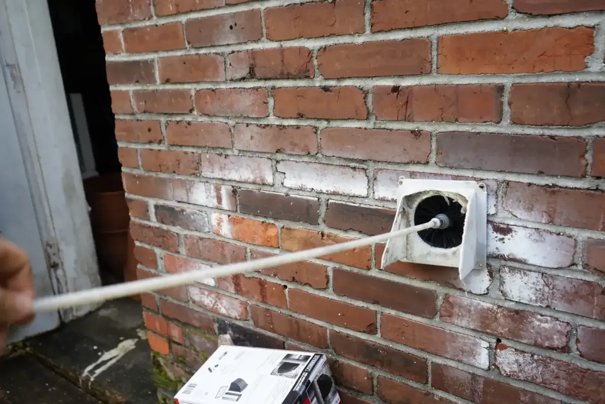 Technician brushing lint from a dryer-vent outlet in Memphis