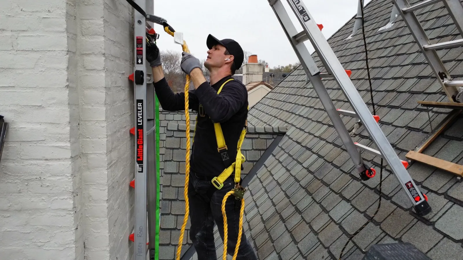 An Abbey Road technician on a roof beside an extension ladder at a white brick chimney