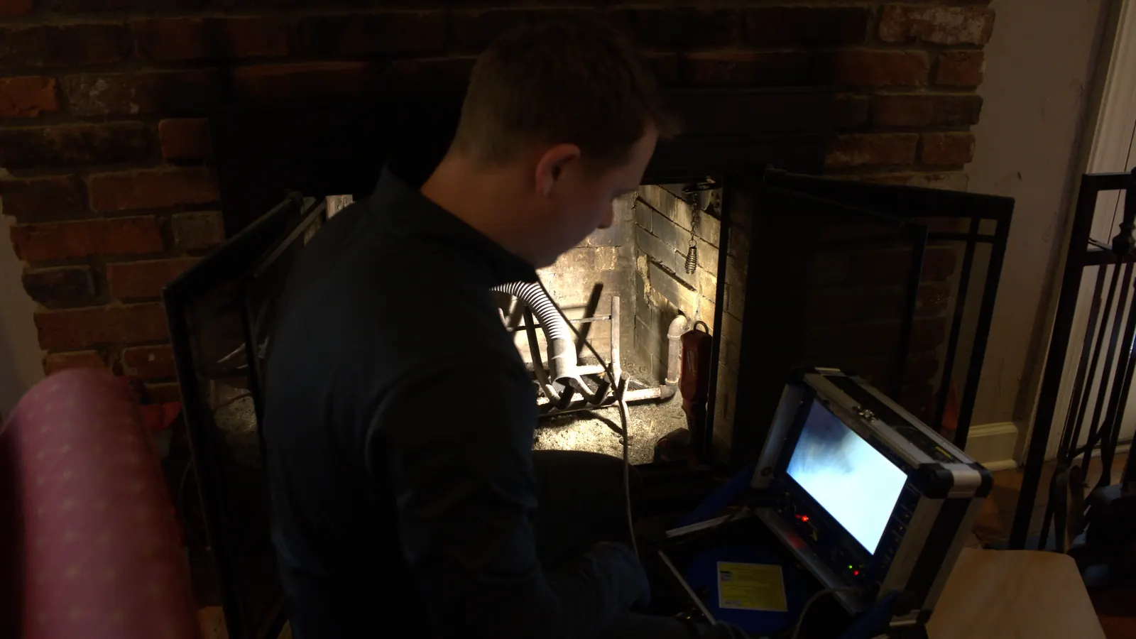 A technician running a camera inspection at an indoor fireplace with the monitor beside him