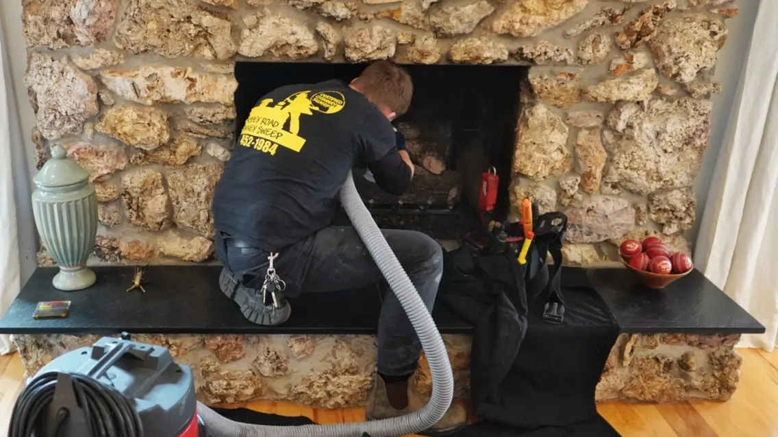 A technician sweeping a stone fireplace with a vacuum hose running to the firebox