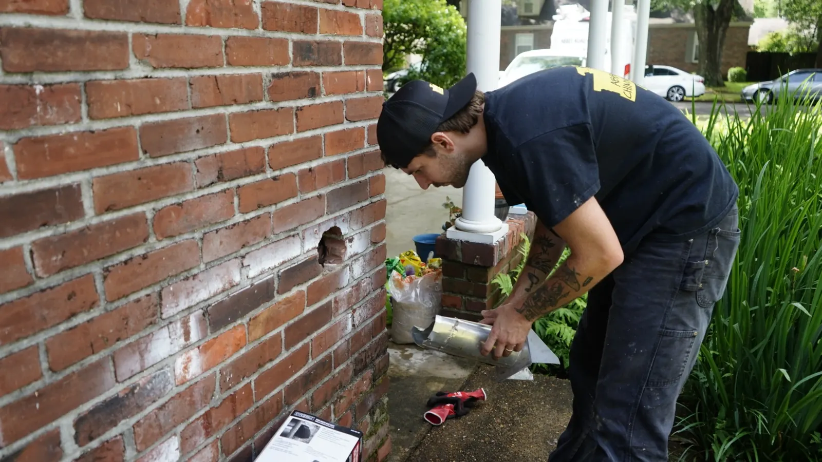 A technician working on a dryer vent outlet at the brick exterior of a Memphis home