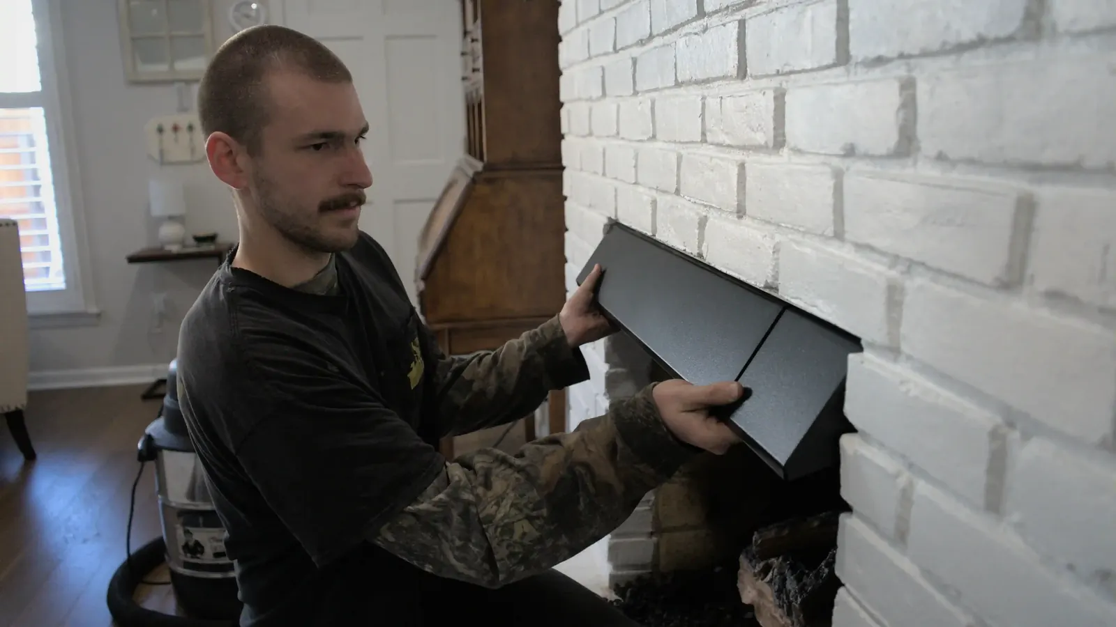 A technician fitting a black surround panel to a white brick fireplace