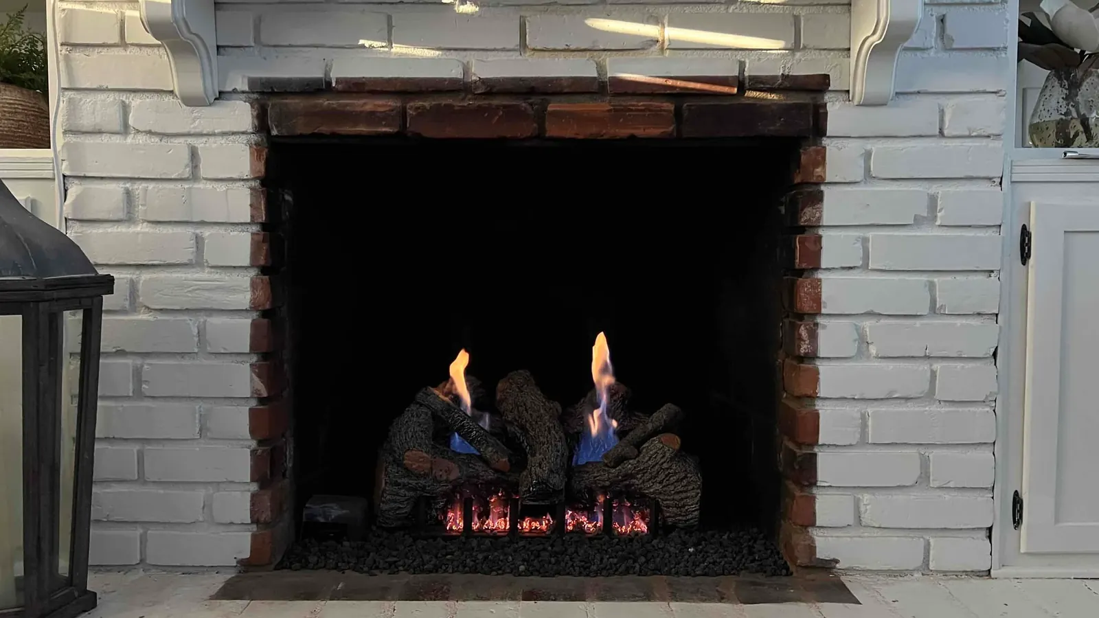A white mantel fireplace with a gas log set alight