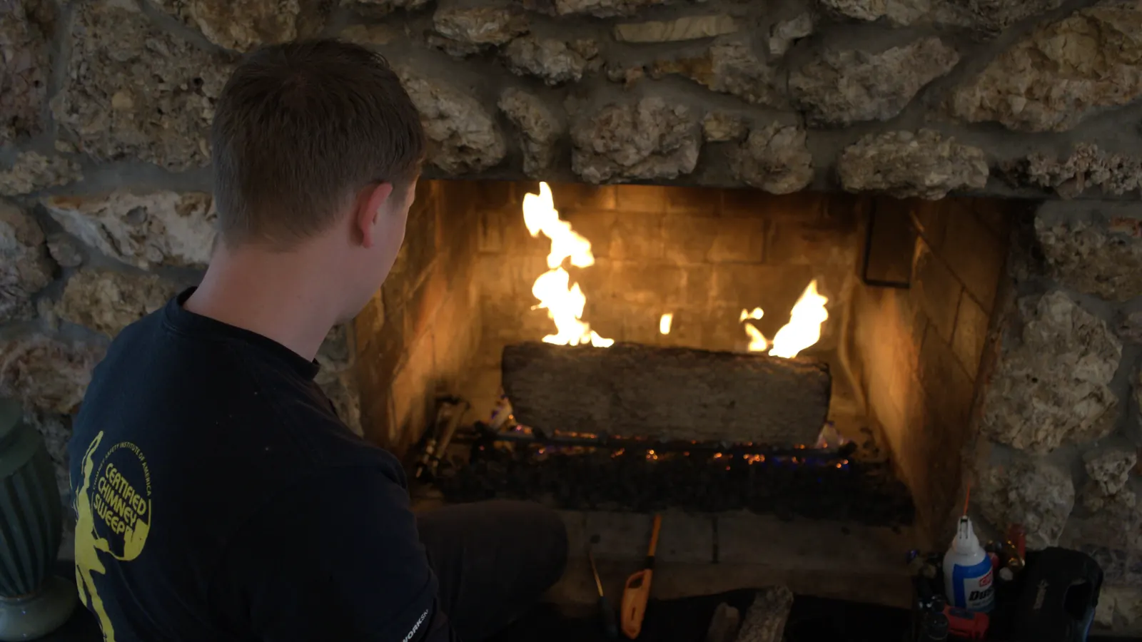 A technician checking the flame pattern on a stone fireplace gas log set